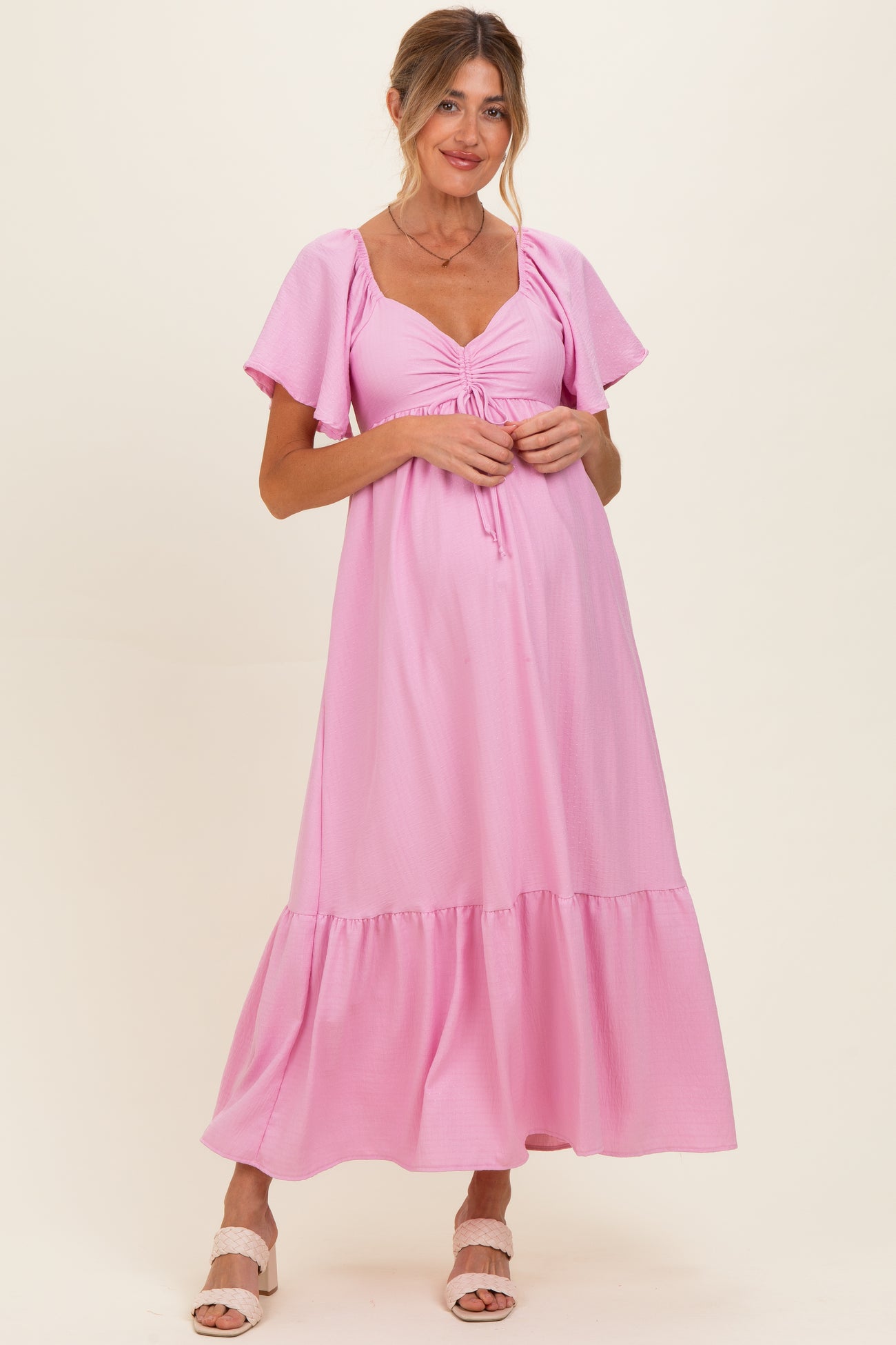 woman wearing a pink maternity maxi dress with short sleeves and gathered detail at the bust, showcasing her baby bump