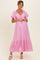 woman wearing a pink maternity maxi dress with short sleeves and gathered detail at the bust, showcasing her baby bump