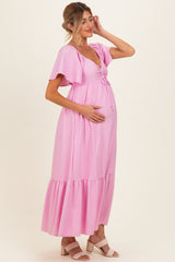 woman wearing a pink maternity maxi dress with flutter sleeves and a drawstring bodice, holding her baby bump
