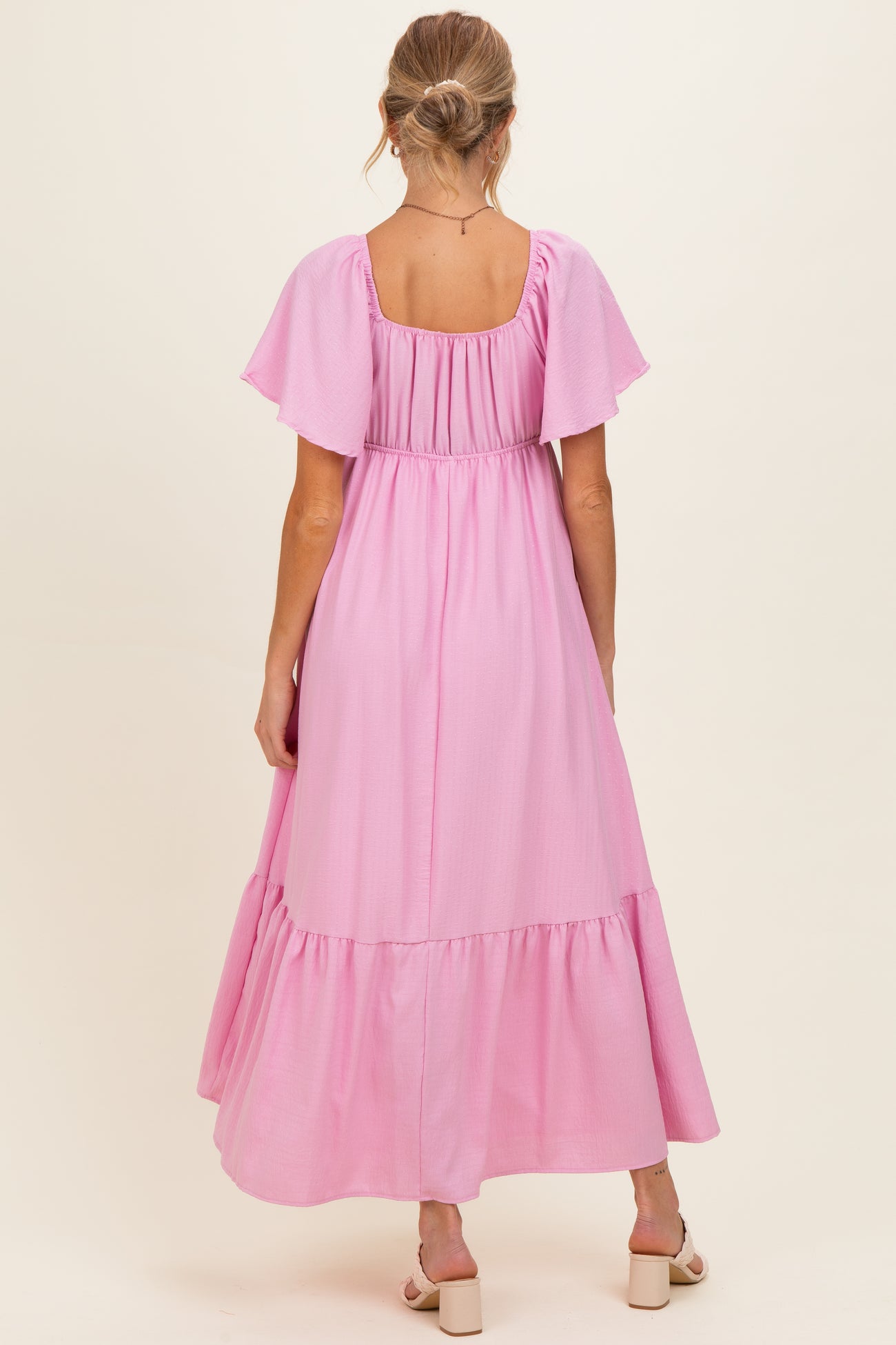 woman wearing a light pink maternity maxi dress with flutter sleeves and a tiered skirt, showing her baby bump from the back