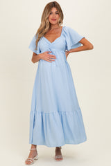 woman wearing a light blue maternity dress with flutter sleeves and a tie front, showing her baby bump