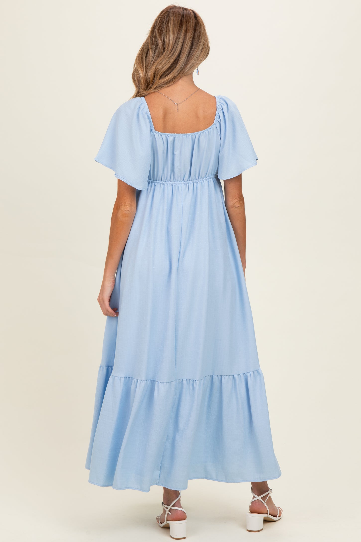 woman wearing a light blue maternity maxi dress with puff sleeves and a tiered skirt, seen from the back