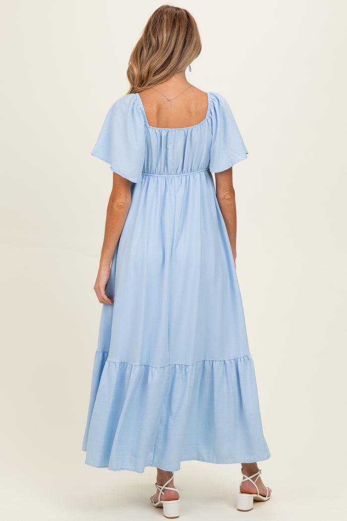 woman wearing a light blue maternity maxi dress with puff sleeves and a tiered skirt, seen from the back