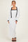 woman wearing a white maxi dress with black trim and a matching cropped jacket, posing with one hand on her hip
