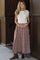 woman wearing a white short sleeve crop top and a brown plaid maxi skirt, gently holding her baby bump