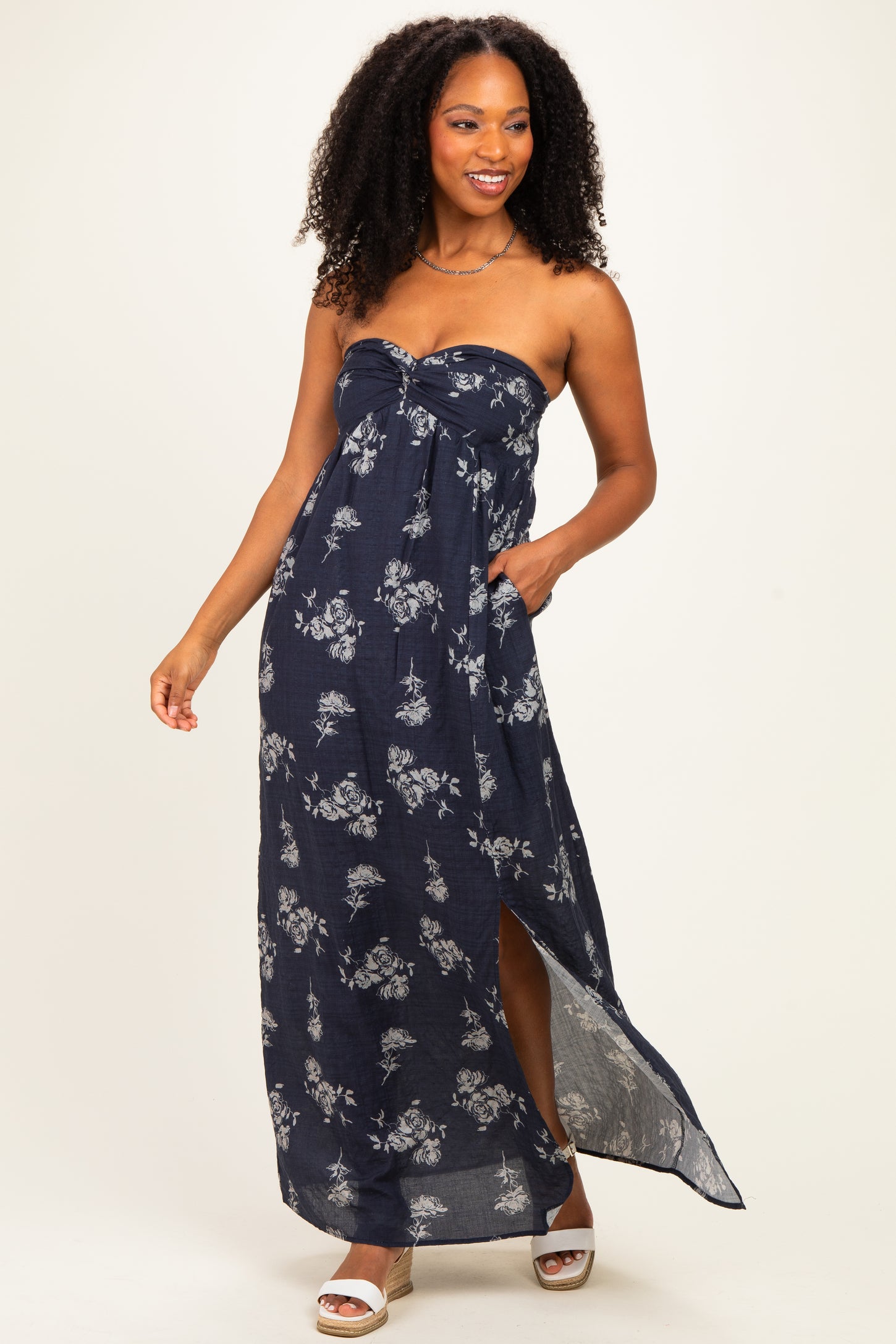 woman wearing a navy floral maxi dress with a strapless design and side slits, standing and smiling