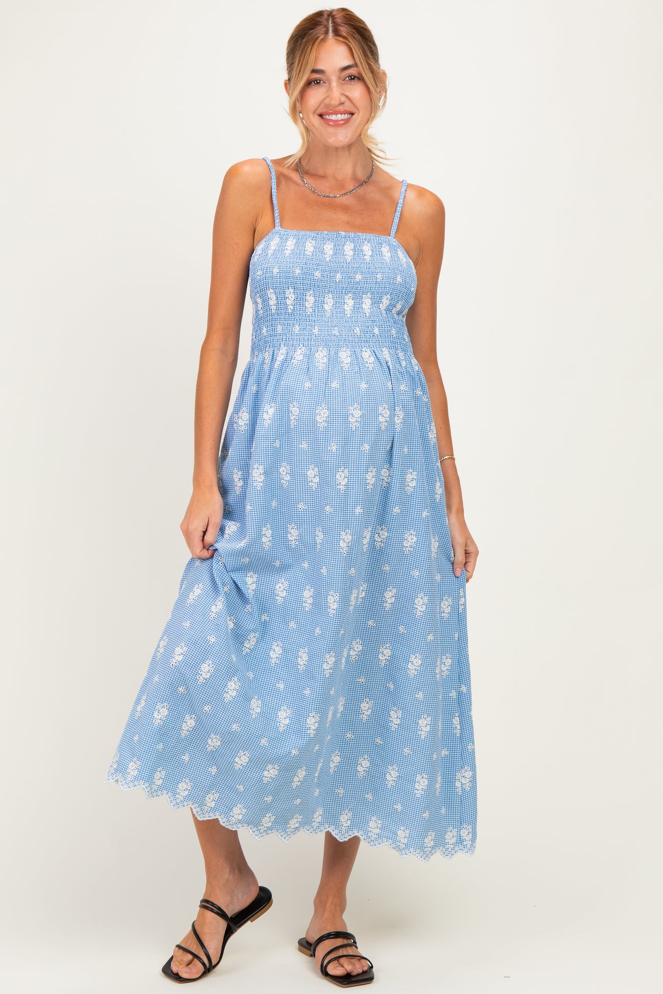 woman wearing a light blue floral maternity dress with a smocked bodice and spaghetti straps, holding her baby bump