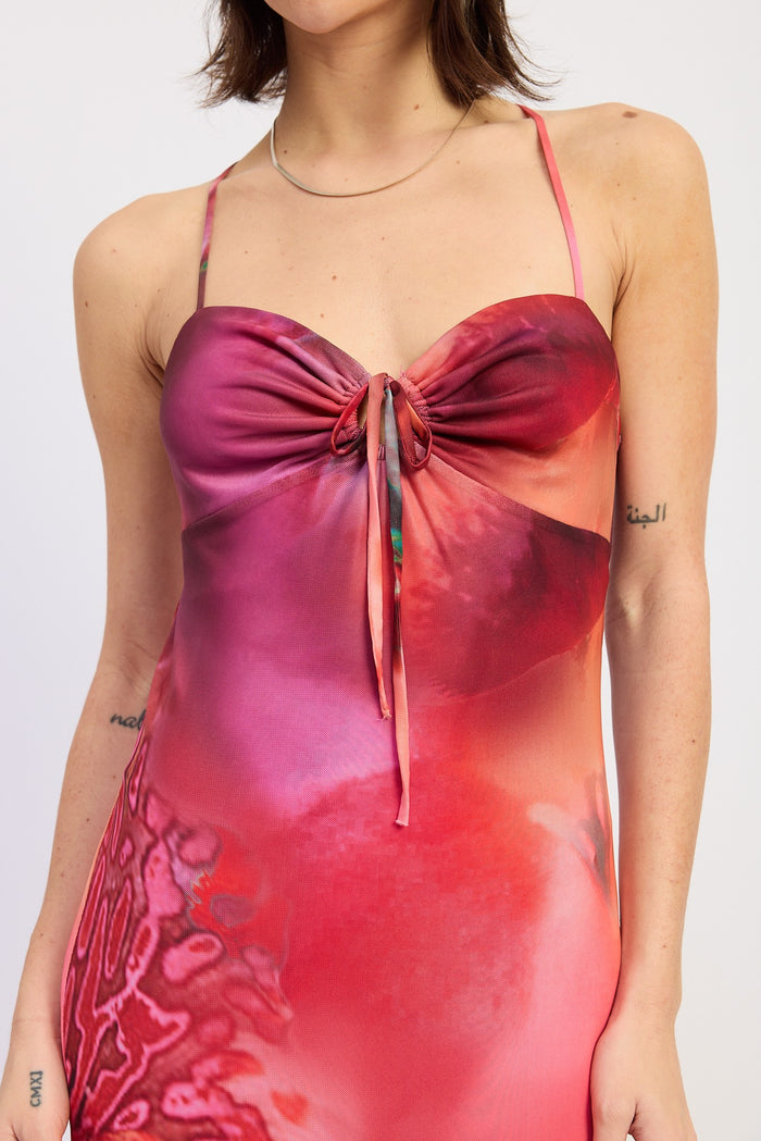 woman wearing a vibrant pink and red tie-front dress with thin straps and a floral design