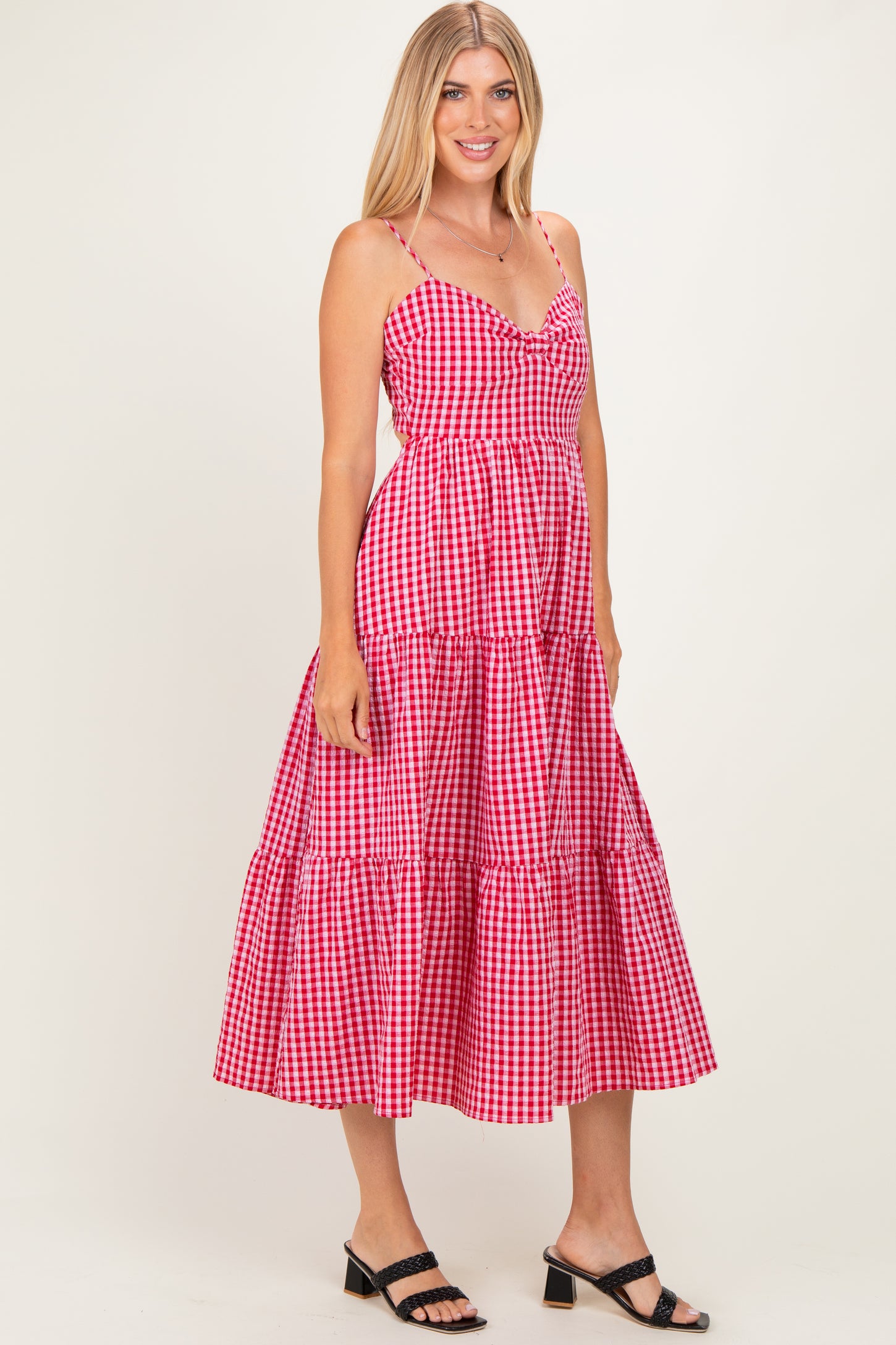 woman wearing a pink and white gingham midi dress with spaghetti straps and a tiered skirt