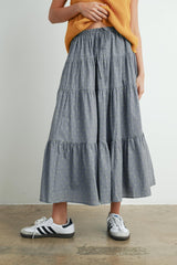 woman wearing a grey tiered maxi skirt with yellow patterns and paired with white sneakers and a mustard knit top