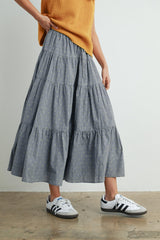 woman wearing a gray tiered midi skirt with yellow polka dots and white sneakers, paired with a relaxed orange sweater