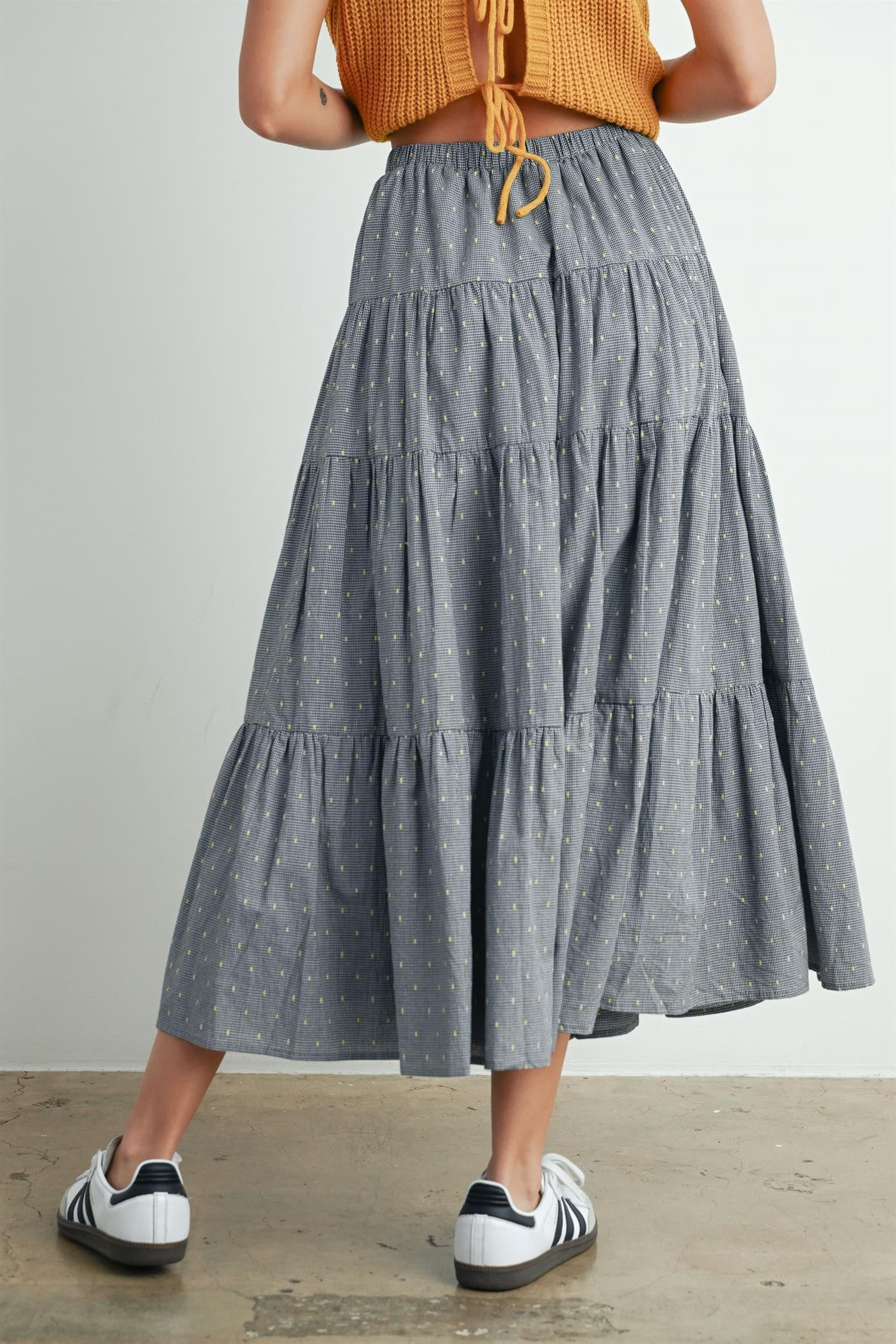 woman wearing a gray tiered maxi skirt with a lightweight fabric and paired with white and black sneakers