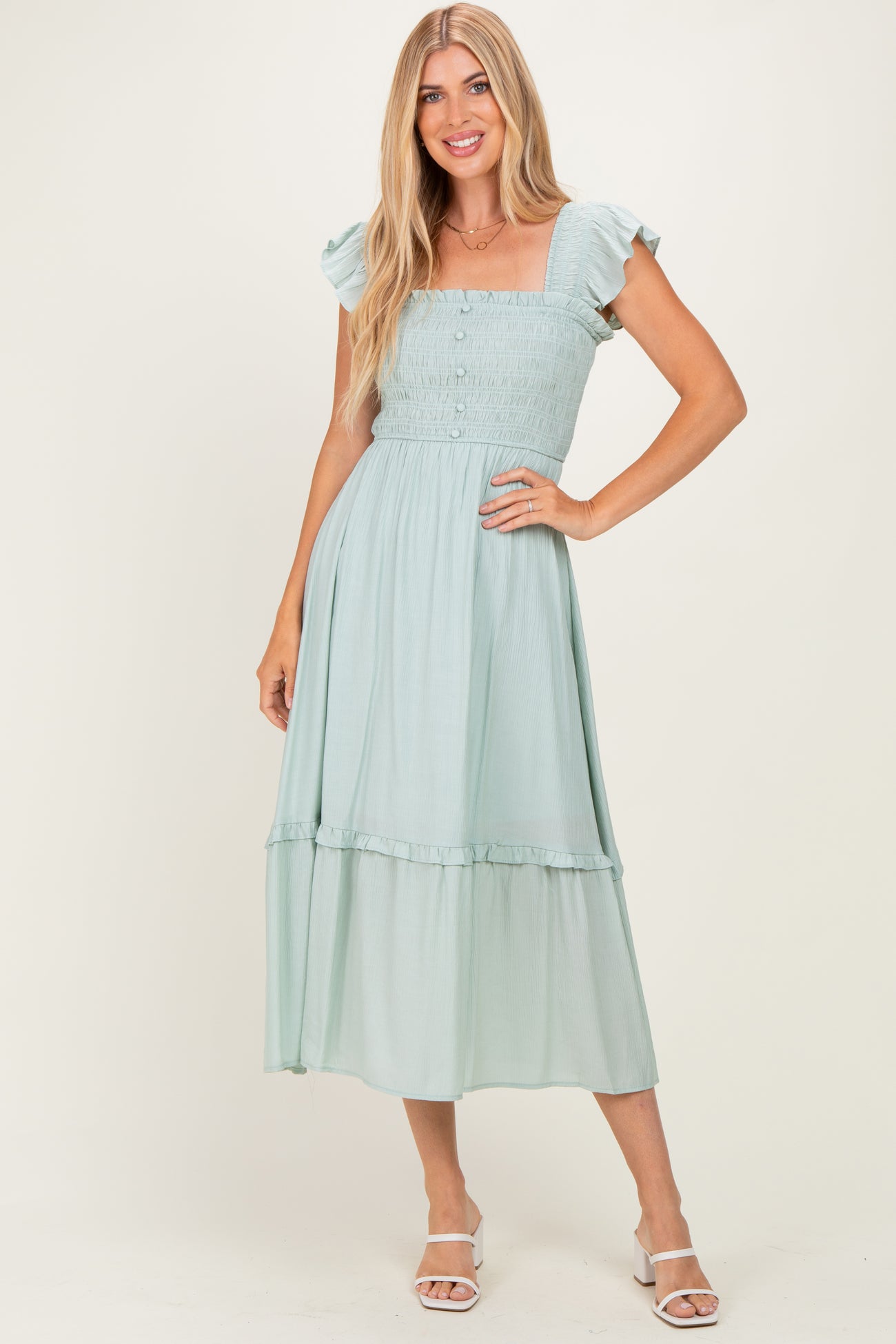 woman wearing a light green midi dress with ruffled sleeves and a fitted bodice, posed on a neutral background