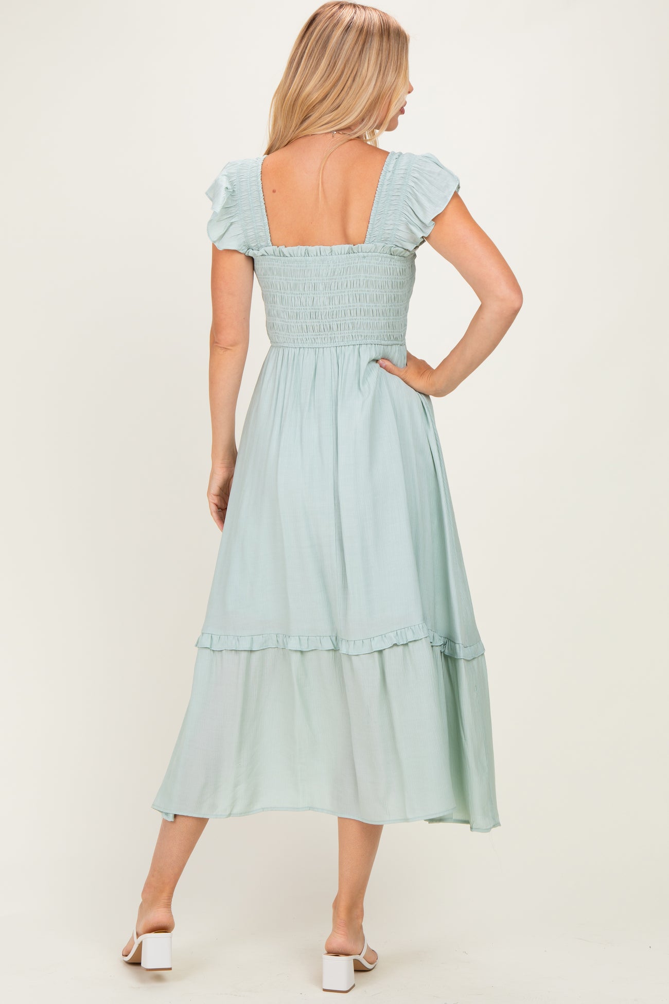woman wearing a light blue smocked back dress with ruffled sleeves and a tiered skirt