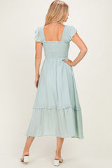 woman wearing a light blue smocked back dress with ruffled sleeves and a tiered skirt