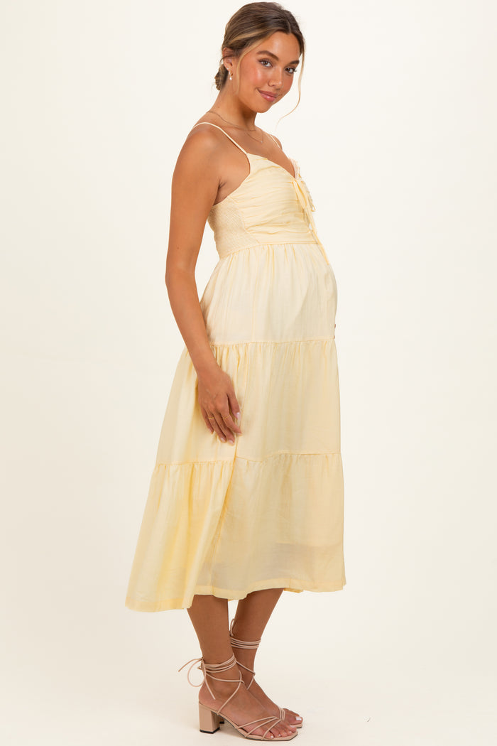 woman wearing a yellow maternity dress with a smocked bodice and tiered skirt, showcasing her baby bump