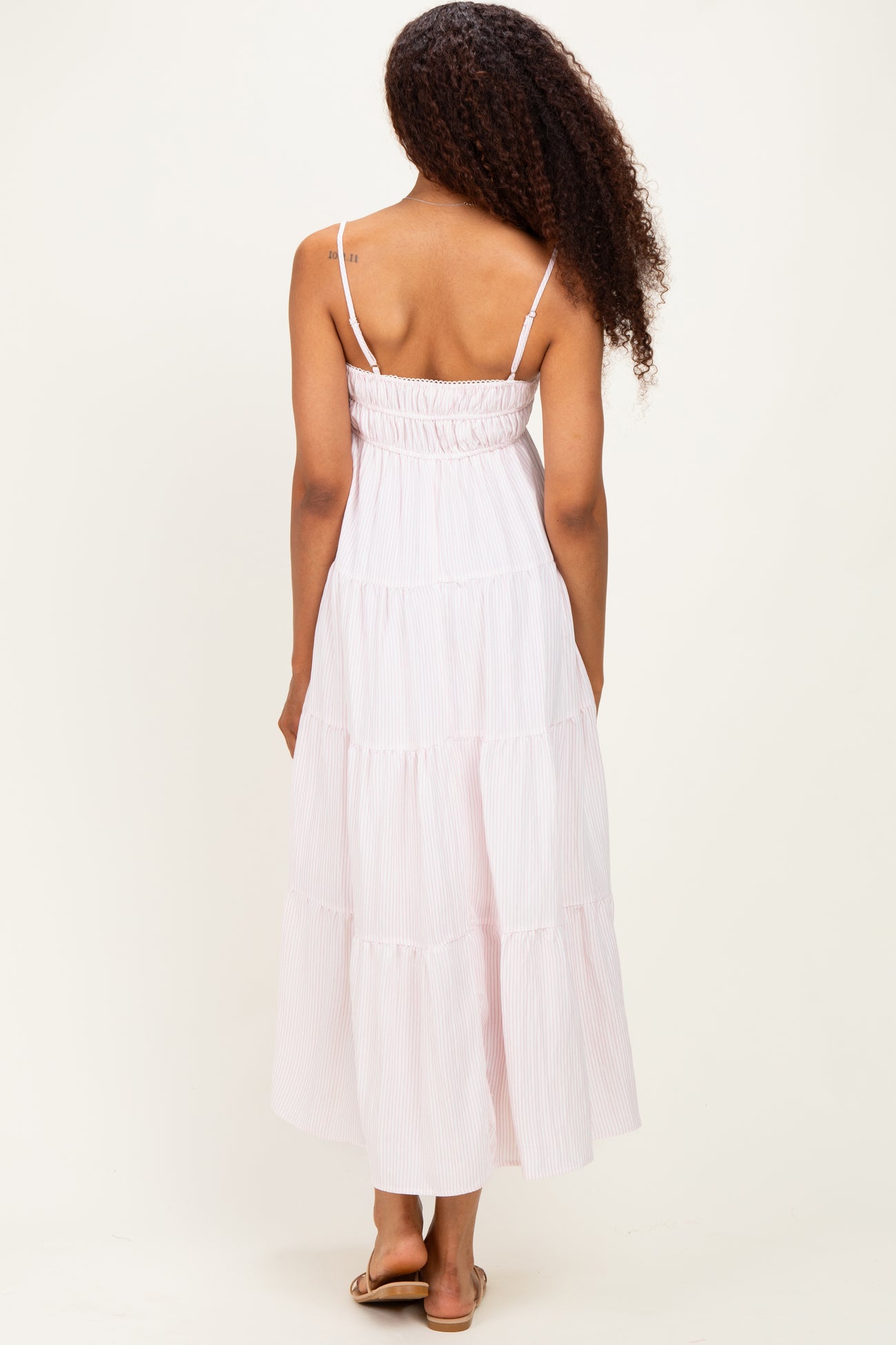 woman wearing a pink and white striped tiered maxi dress with spaghetti straps, showing the back view