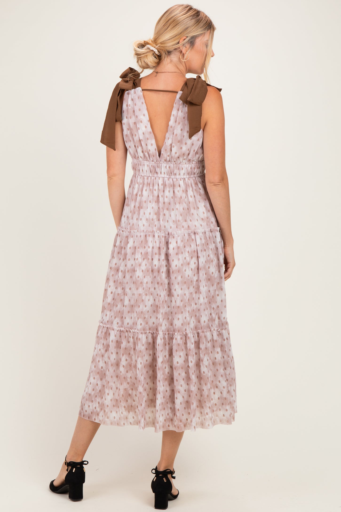 woman wearing a floral midi dress with v-back and bow tie straps in light pink and brown colors