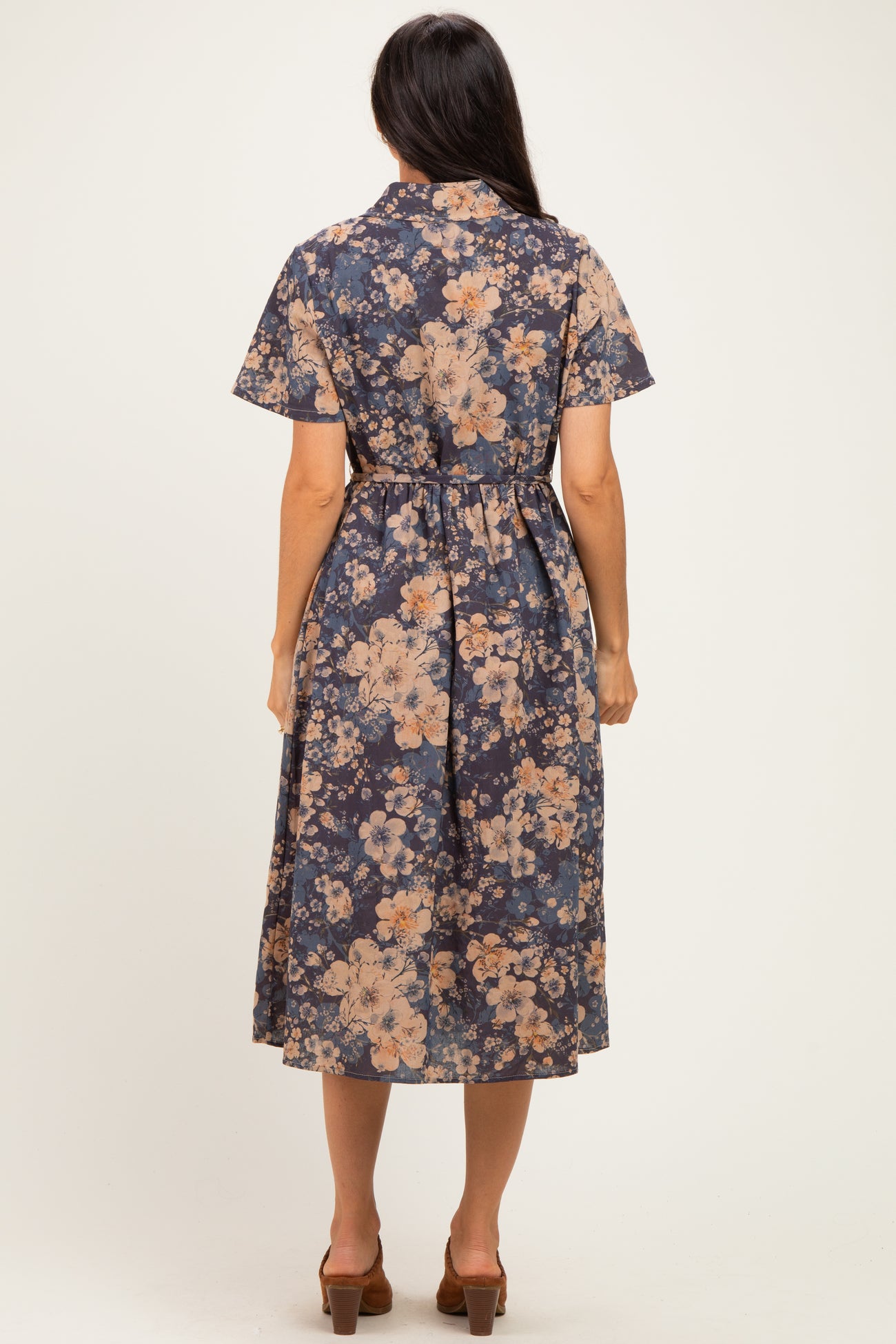 woman wearing a navy floral midi dress with short sleeves and a belted waist, viewed from the back