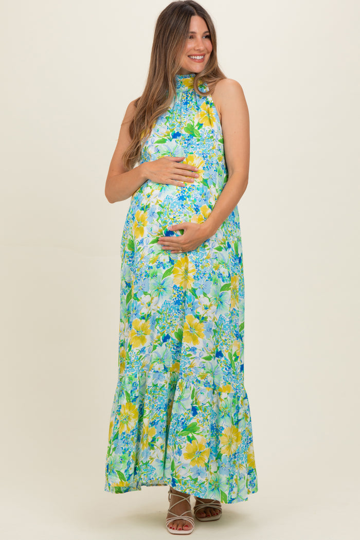 woman wearing a floral maternity maxi dress in shades of blue and yellow, holding her baby bump