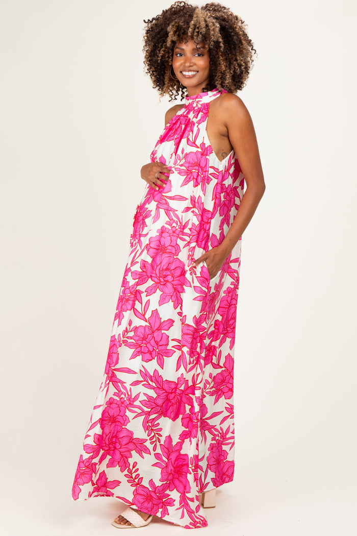 woman wearing a floral pink maternity maxi dress with a halter neck and pockets, showcasing her baby bump