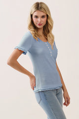 woman wearing a light blue short sleeve textured top with buttons and ruffled edges