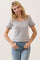 woman wearing a light gray short sleeve henley top with button details and ruffled cuffs, paired with blue jeans