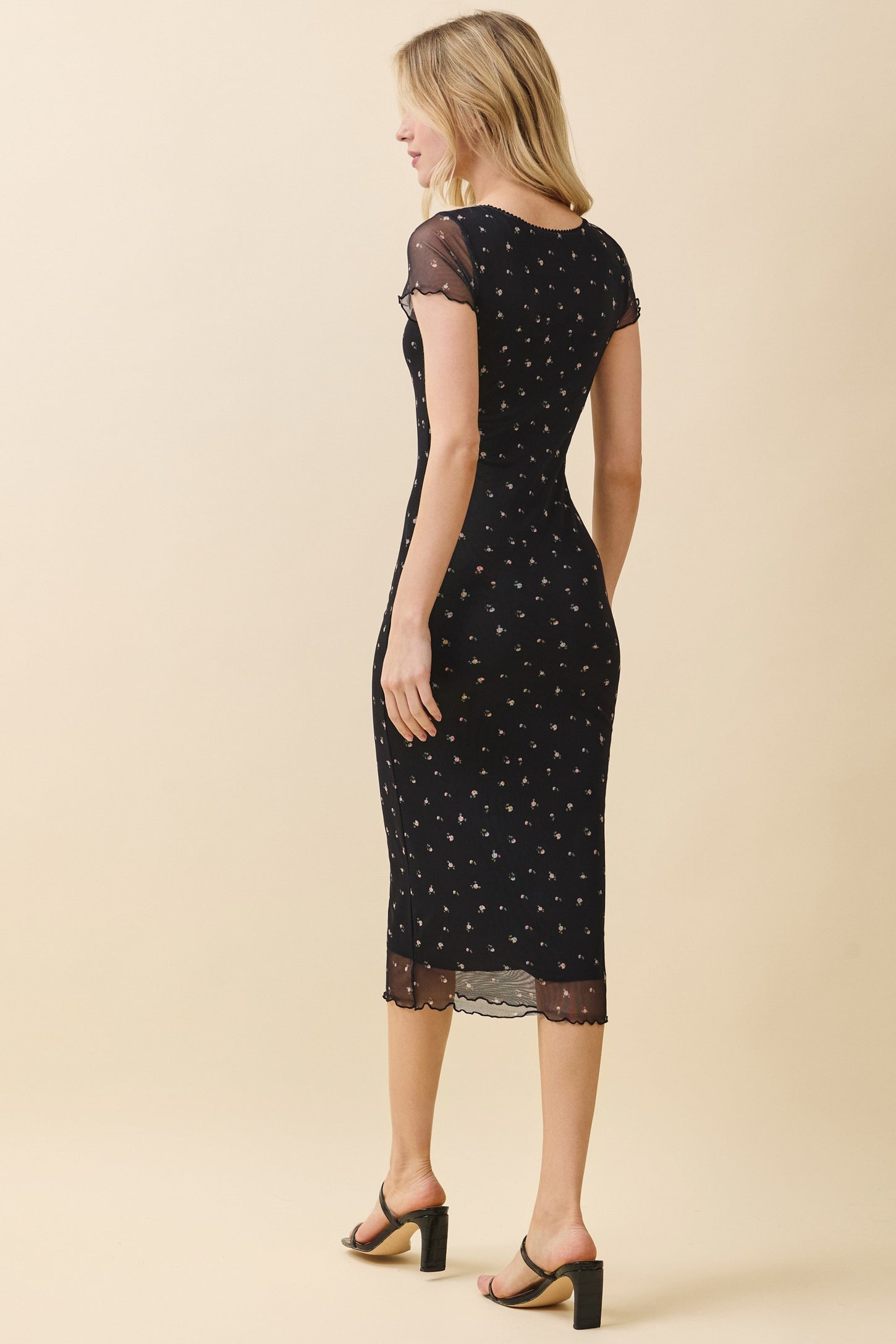 woman wearing a black fitted midi dress with floral patterns and cap sleeves, showing the back view