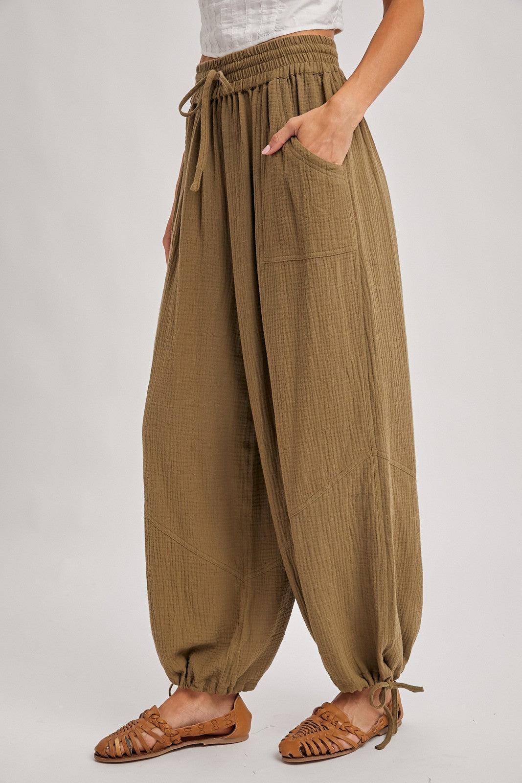 woman wearing olive green loose-fit harem pants with an elastic waistband and pockets, paired with brown strappy sandals