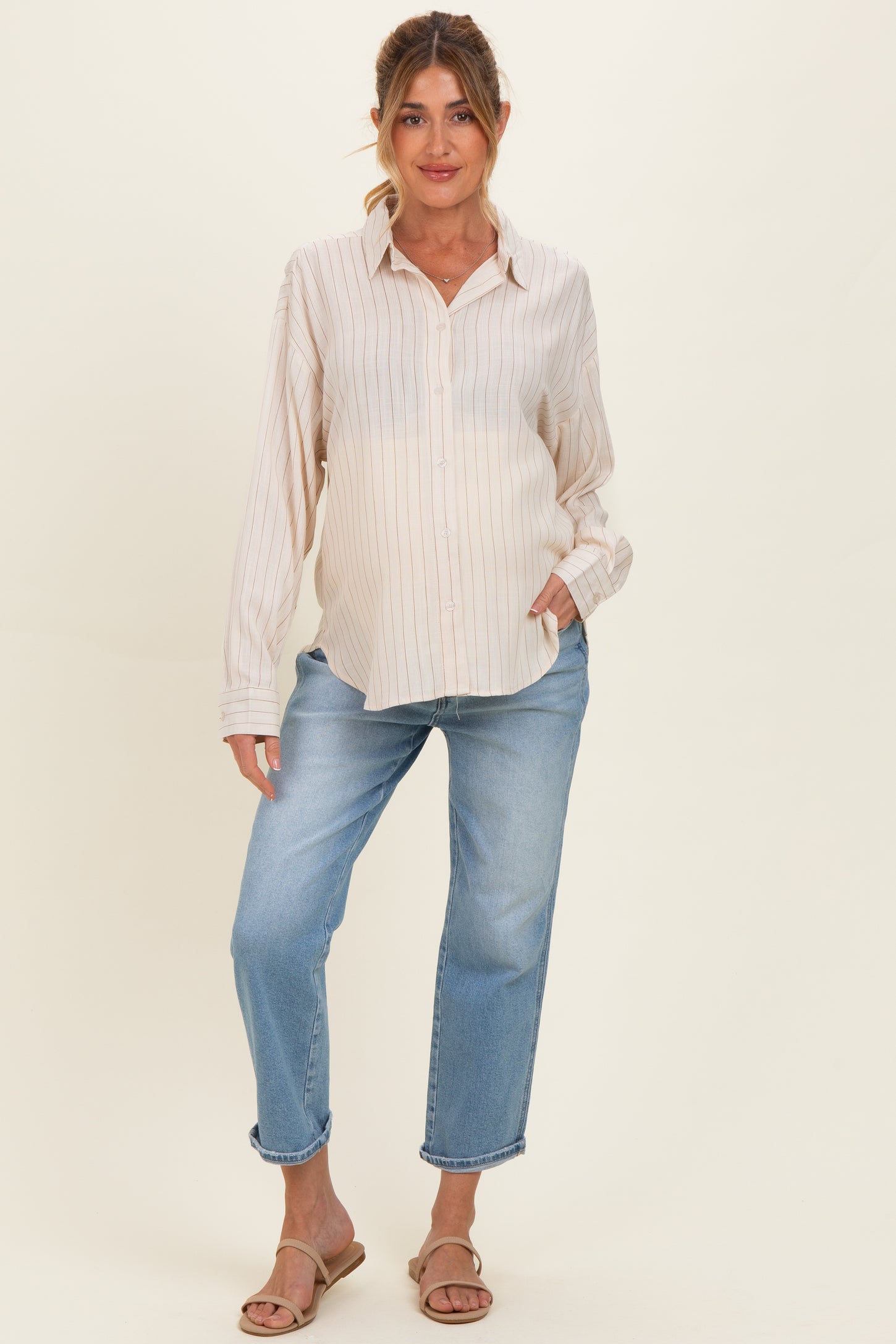 woman wearing a striped maternity button-up shirt and blue maternity jeans, highlighting her baby bump