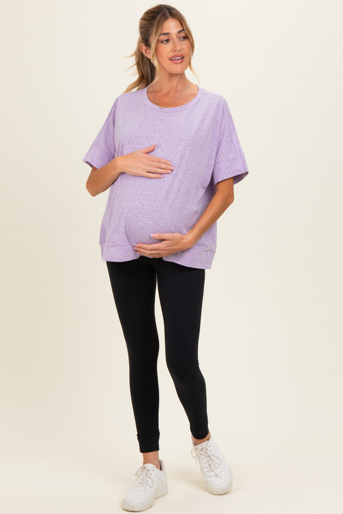 woman wearing a purple oversized maternity t-shirt and black leggings, holding her baby bump