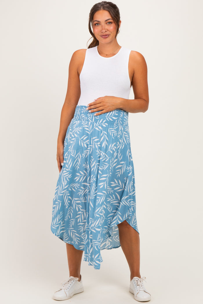 woman wearing a white sleeveless maternity top and a blue patterned maternity skirt, holding her baby bump