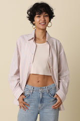 woman wearing a light pink striped oversize shirt over a cropped cream top and high-waisted jeans