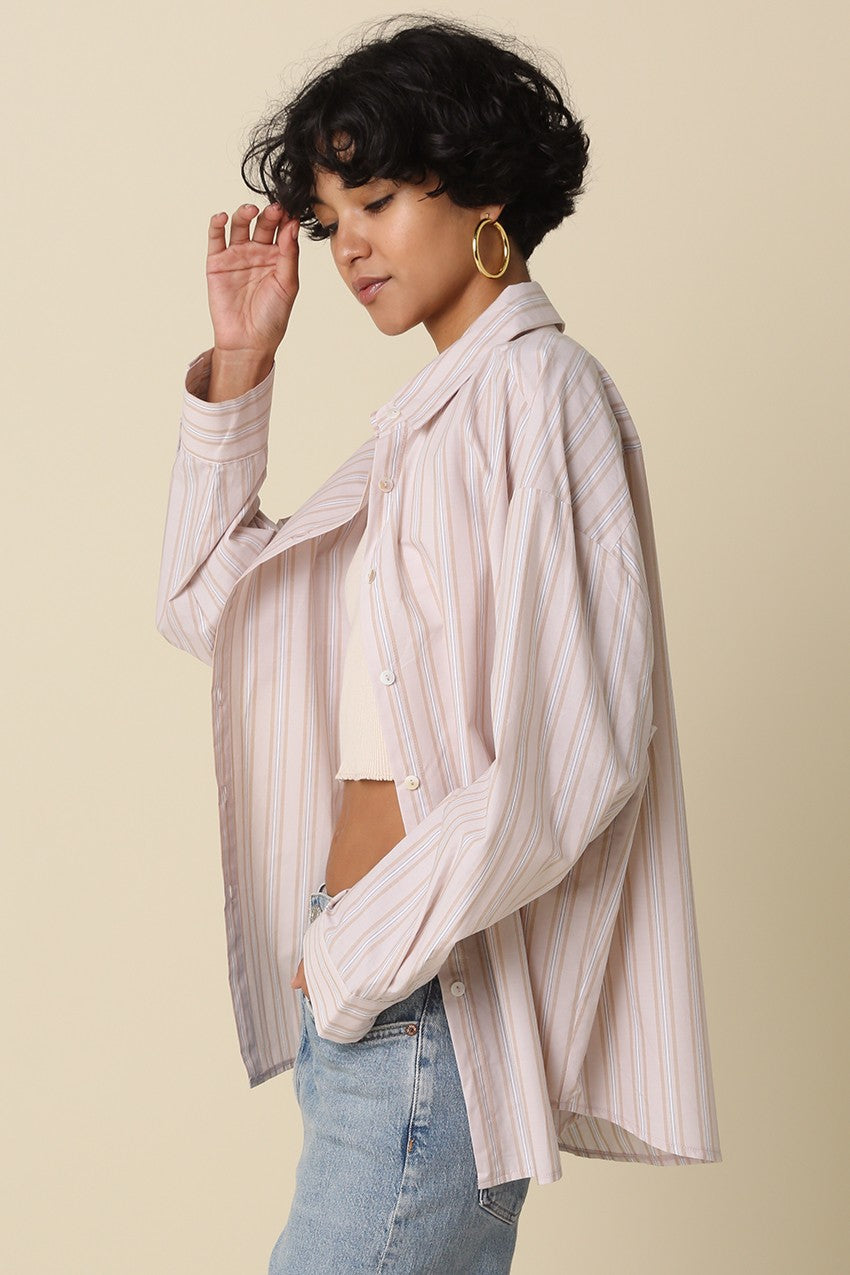 woman wearing a light pink and white striped oversized button-up shirt paired with a crop top and blue jeans