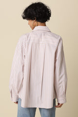 woman wearing a light pink and white striped oversized shirt with a back pleat, paired with light blue jeans