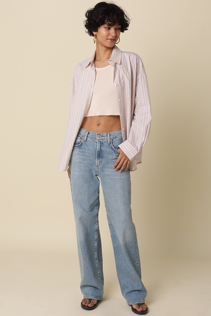 woman wearing a light pink striped oversized shirt and a fitted cropped top with high-waisted blue jeans