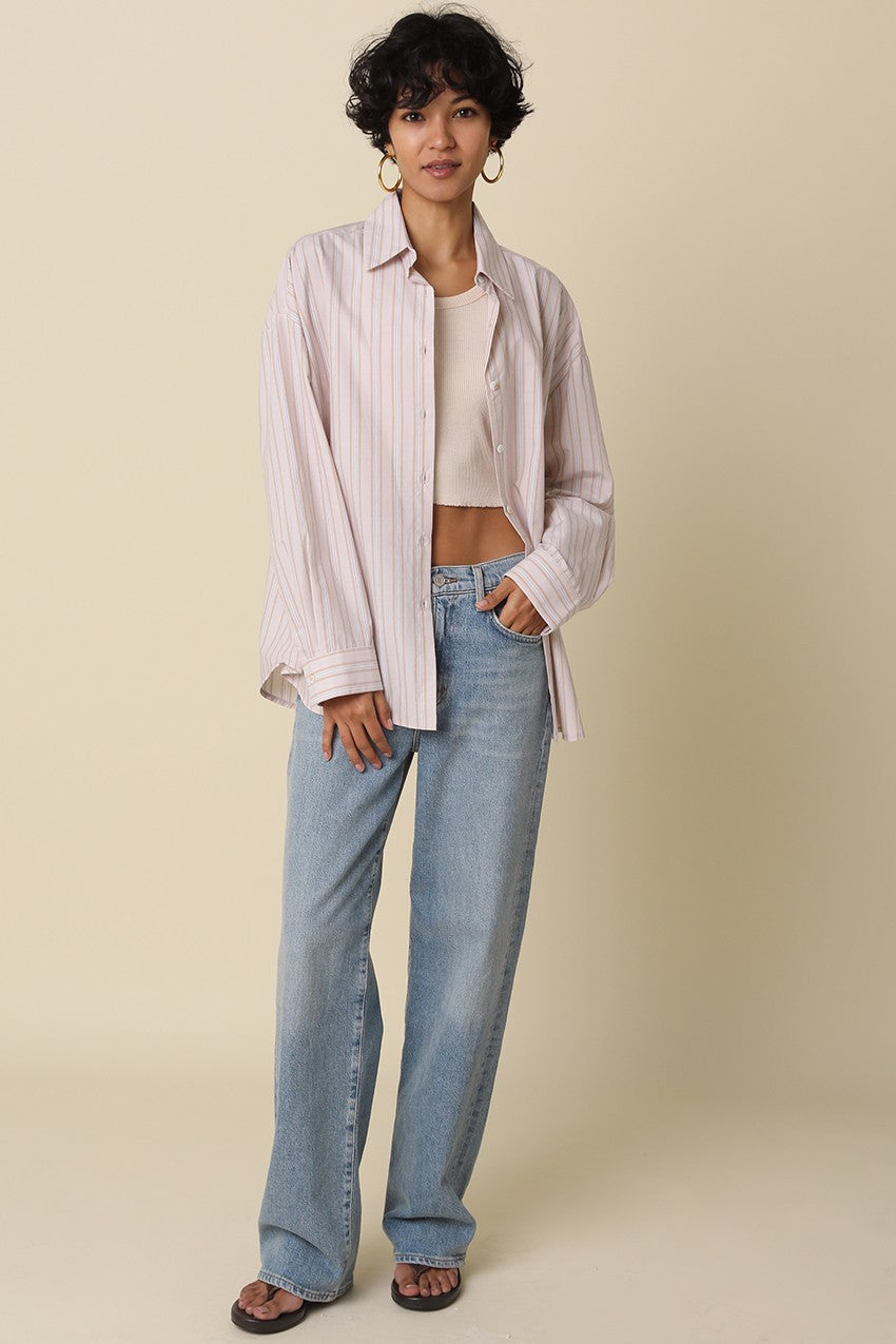 woman wearing a pastel striped button-up shirt over a cropped tank top and blue wide-leg jeans