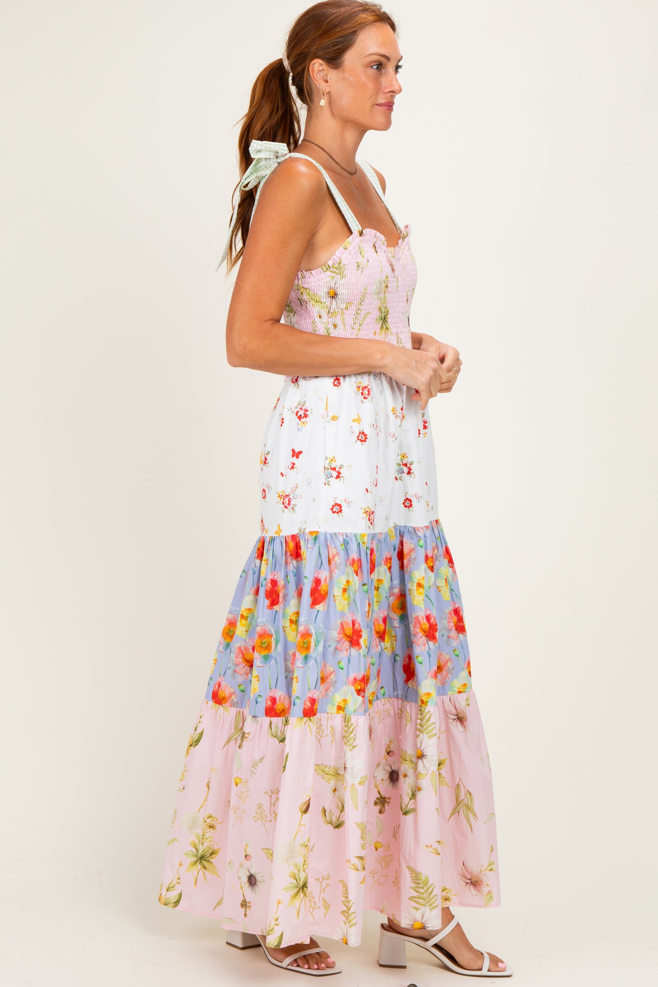 woman wearing a floral maxi dress with a fitted bodice and tiered skirt in various pastel colors and floral patterns