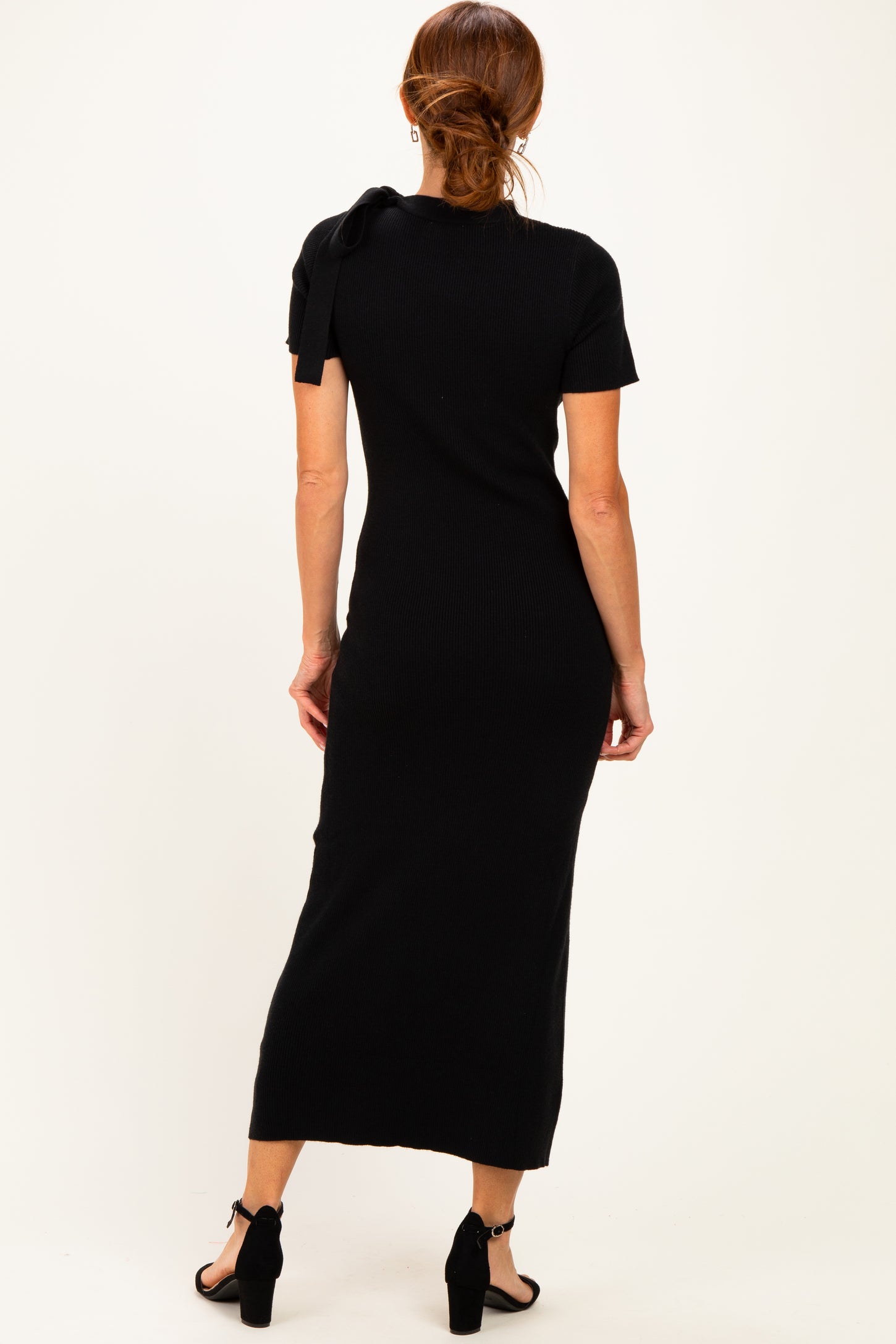 woman wearing a black ribbed midi dress with short sleeves and a bow detail on the shoulder, viewed from the back