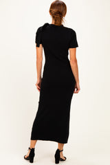 woman wearing a black ribbed midi dress with short sleeves and a bow detail on the shoulder, viewed from the back