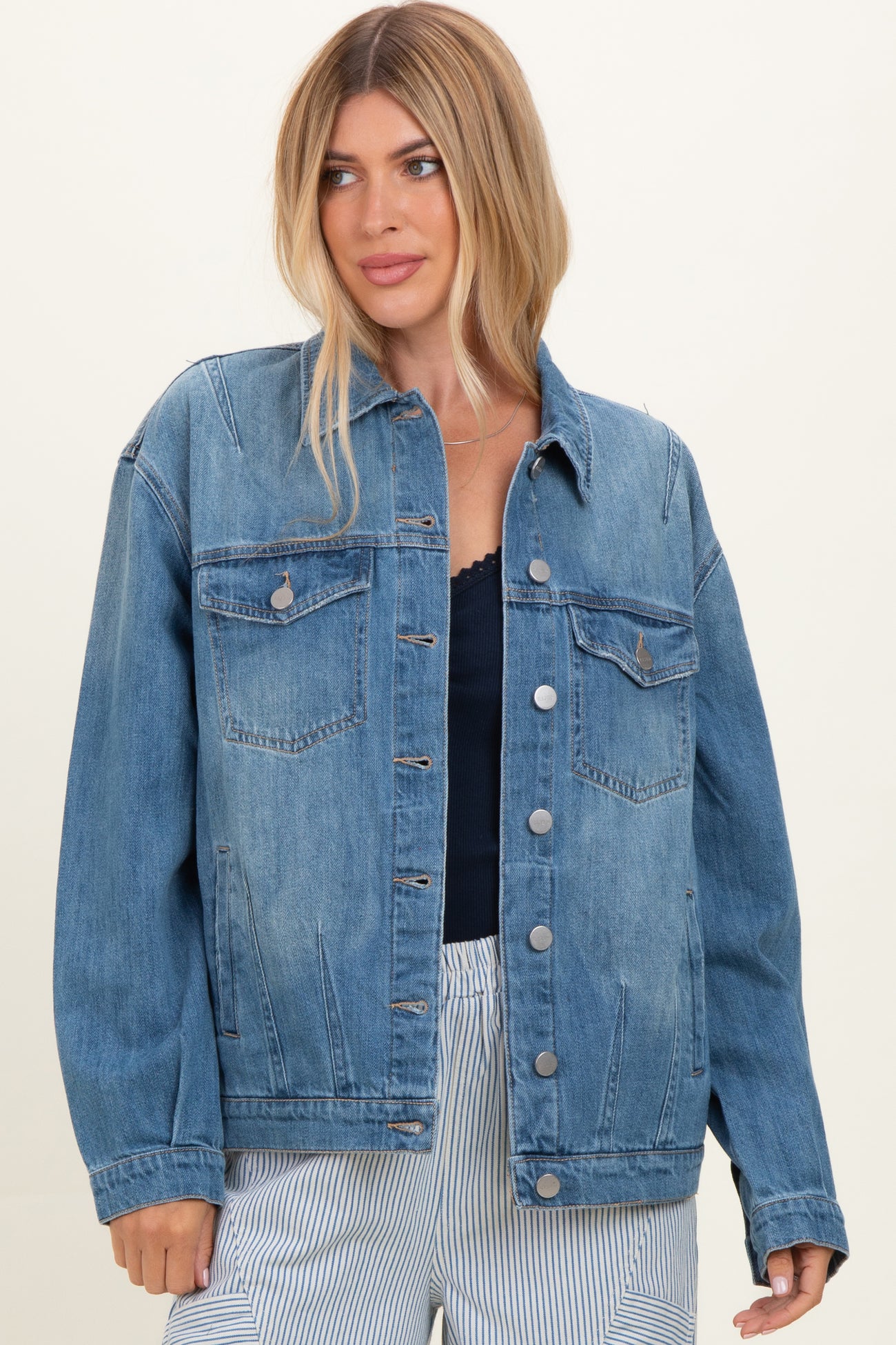 woman wearing a light wash denim jacket with front pockets and button closure, styled with a navy top and striped pants
