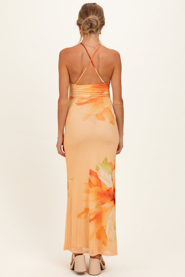 woman wearing a back view of an orange floral maternity maxi dress with a fitted silhouette and crisscross straps