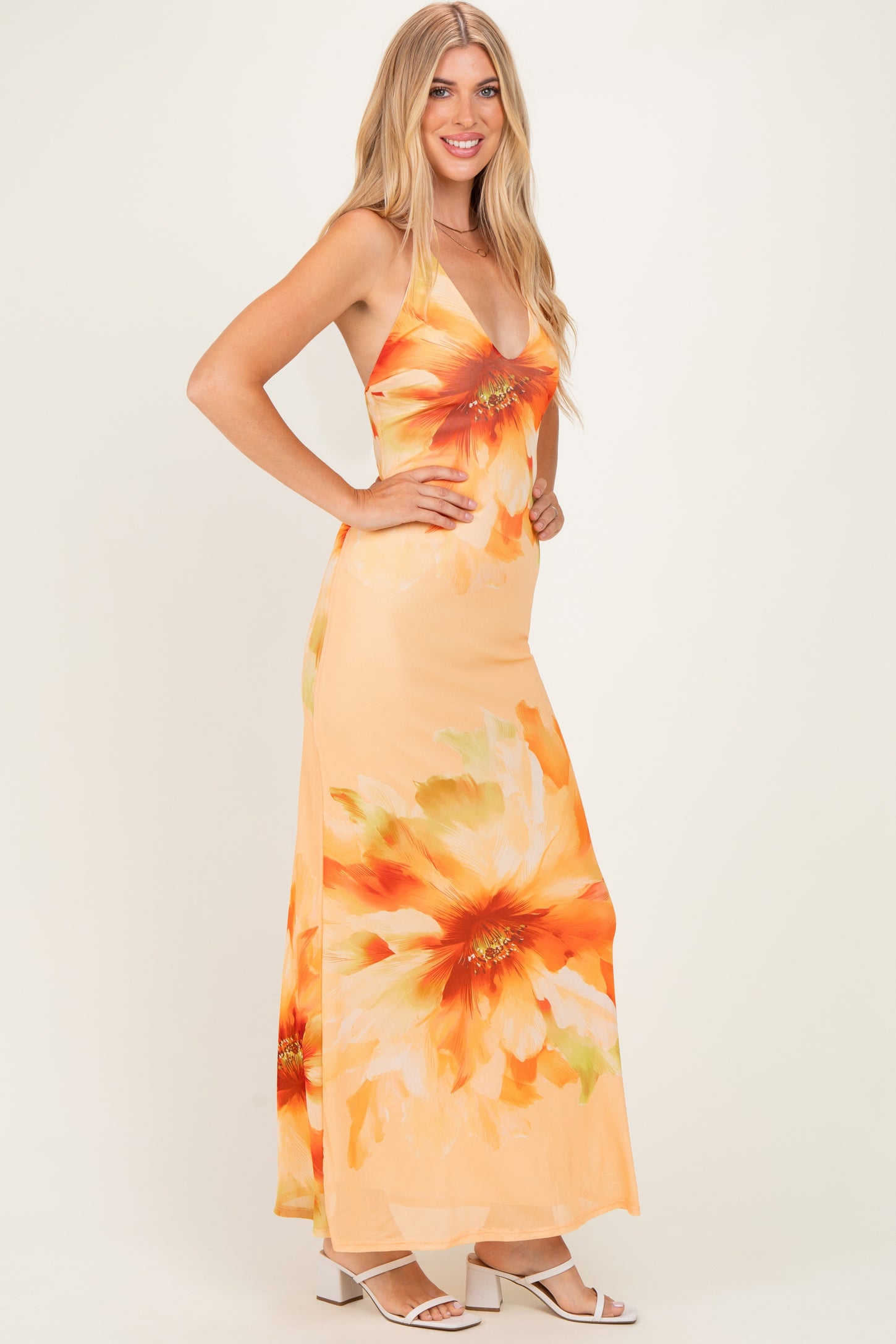 woman wearing a peach maxi dress with large orange floral print and a deep V-neckline