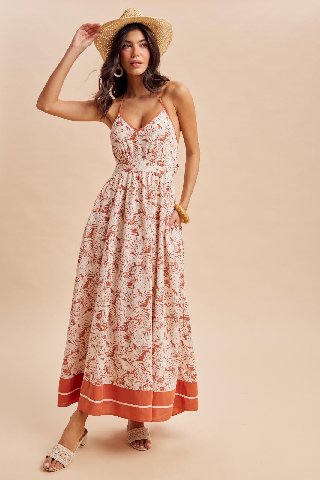 woman wearing a patterned maxi dress with spaghetti straps and a cinched waist, styled with a straw hat and sandals