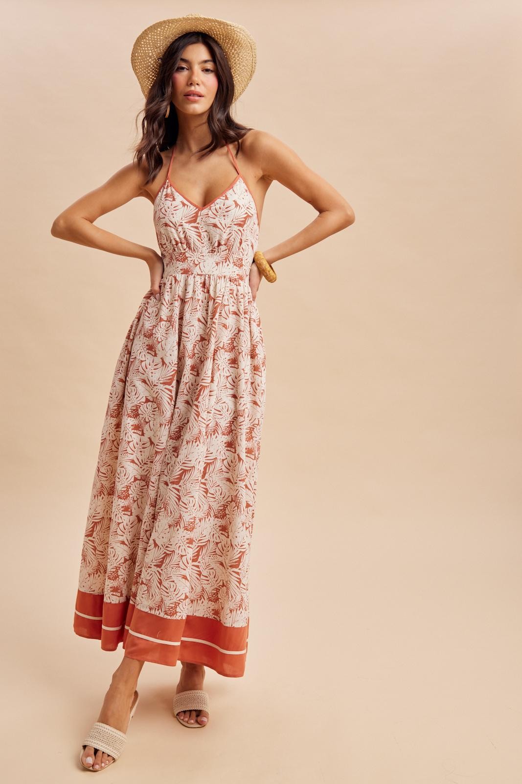 woman wearing a floral maxi dress with a halter neck and a tiered hem, styled with a straw hat and sandals