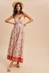 woman wearing a floral maxi dress with a halter neck and a tiered hem, styled with a straw hat and sandals