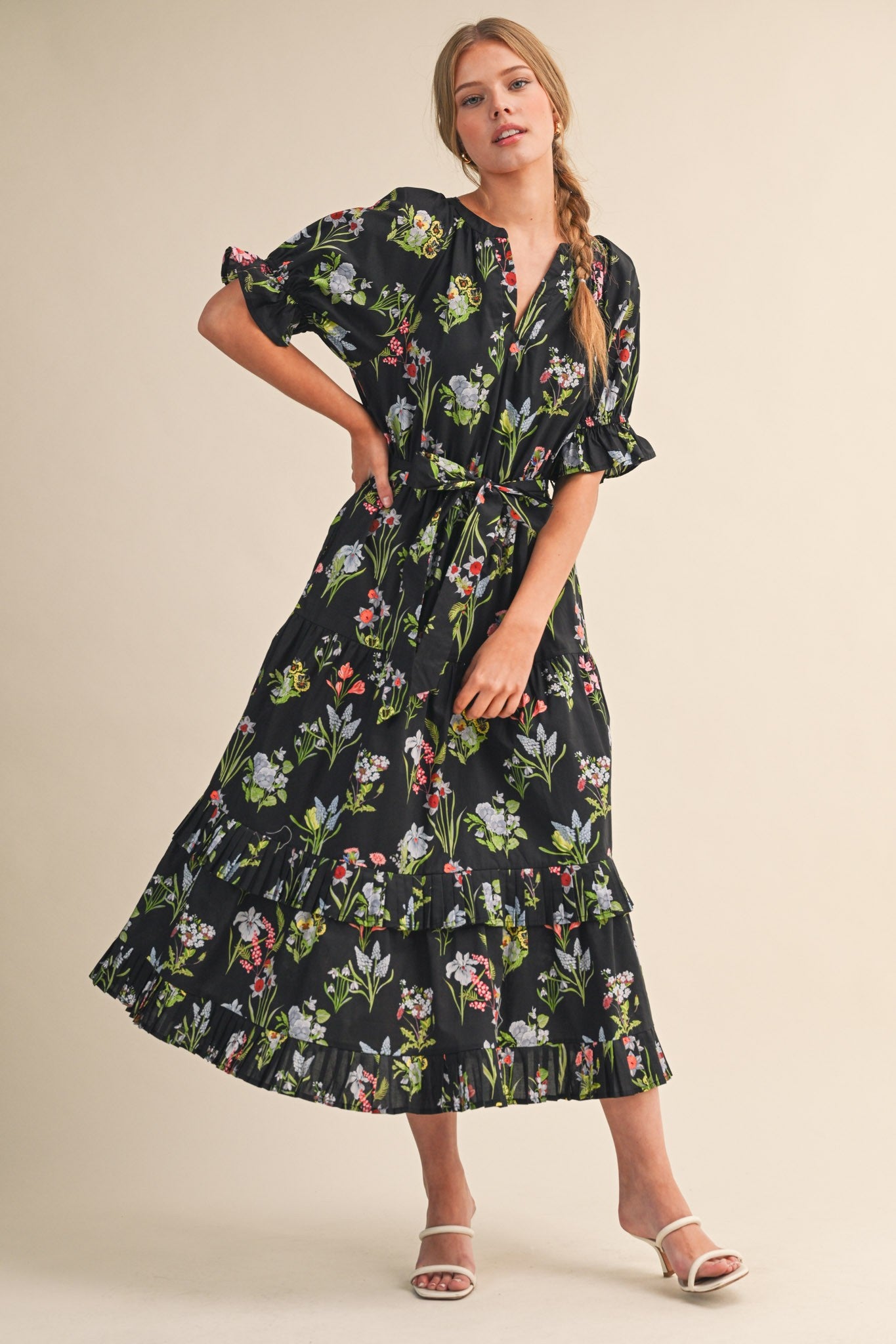 woman wearing a black floral maxi dress with short sleeves and a tiered skirt, posing with a hand on her hip