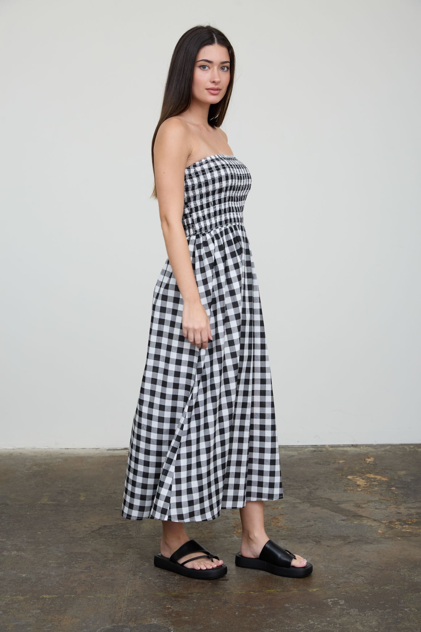woman wearing a black and white gingham strapless maxi dress and black slide sandals