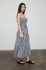 woman wearing a black and white gingham strapless maxi dress and black slide sandals