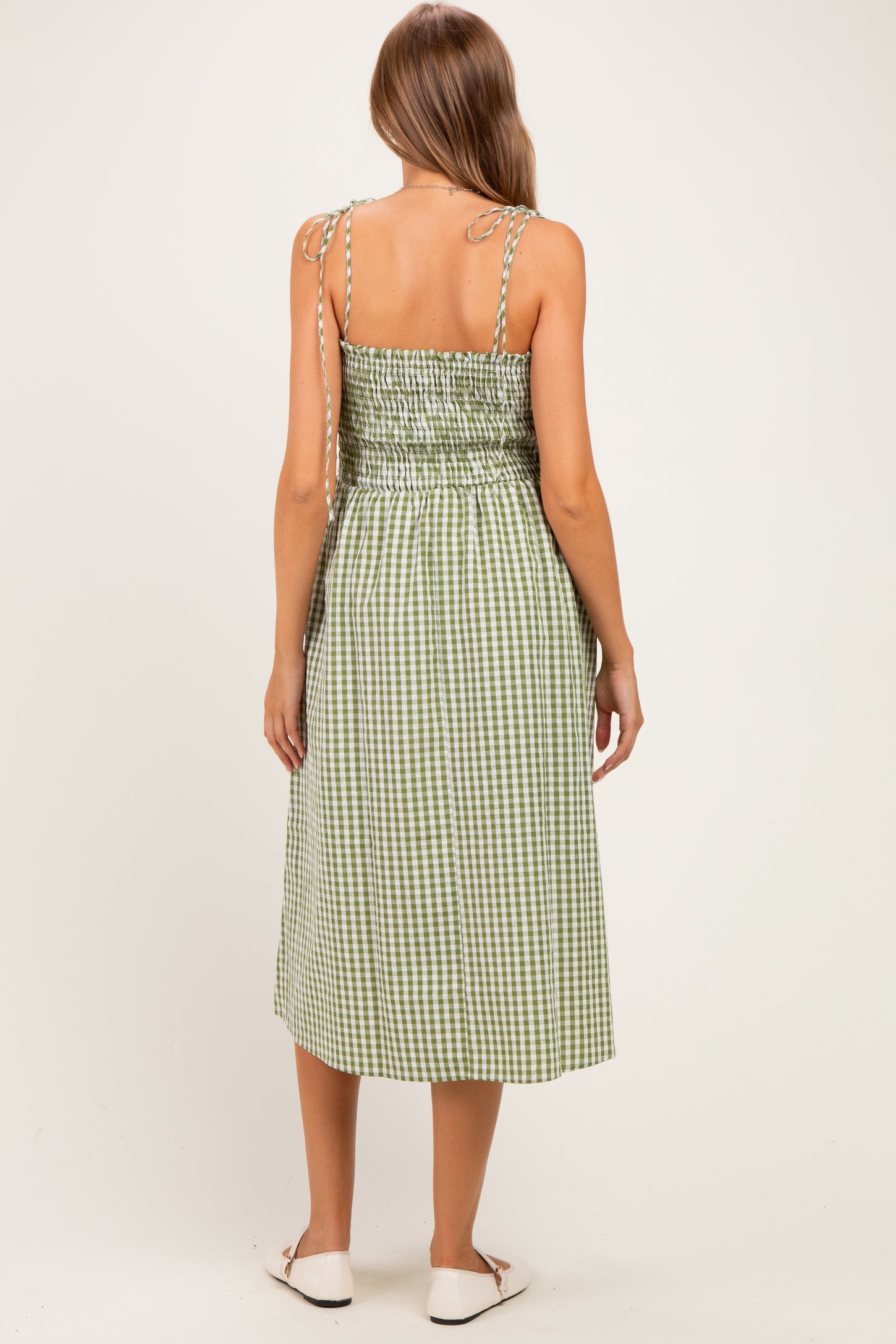 woman wearing a green and white gingham maternity dress with adjustable straps and a smocked back